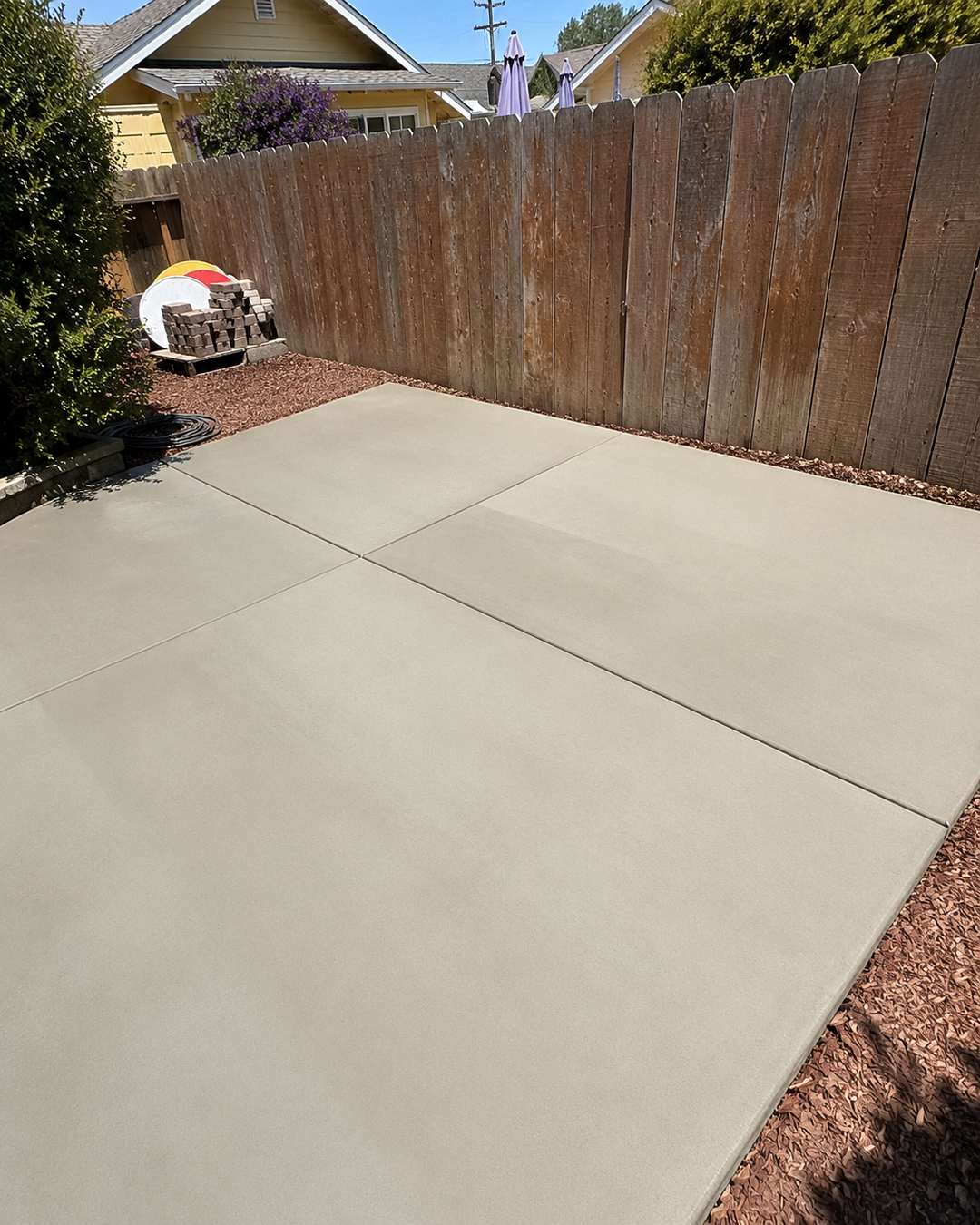 Smooth-finish backyard concrete patio beside a wood privacy fence