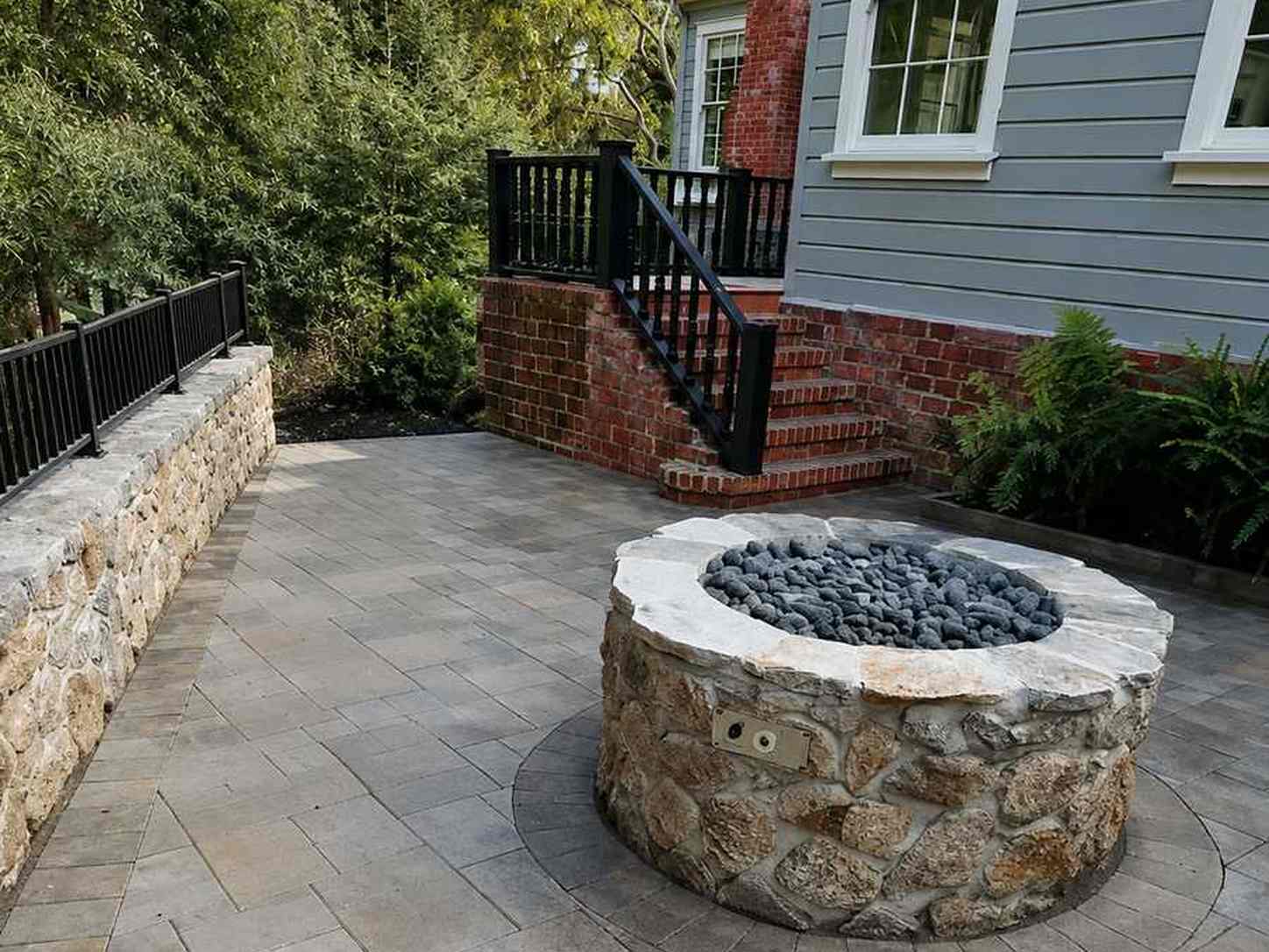 Stone fire pit surrounded by a paver patio, masonry walls, and brick steps