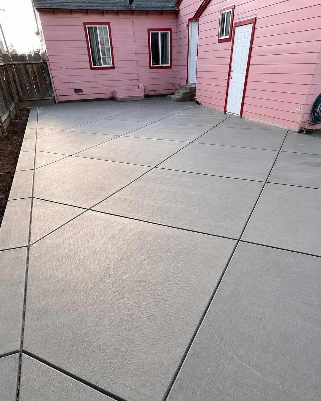 Large concrete patio with evenly spaced control joints beside a pink home